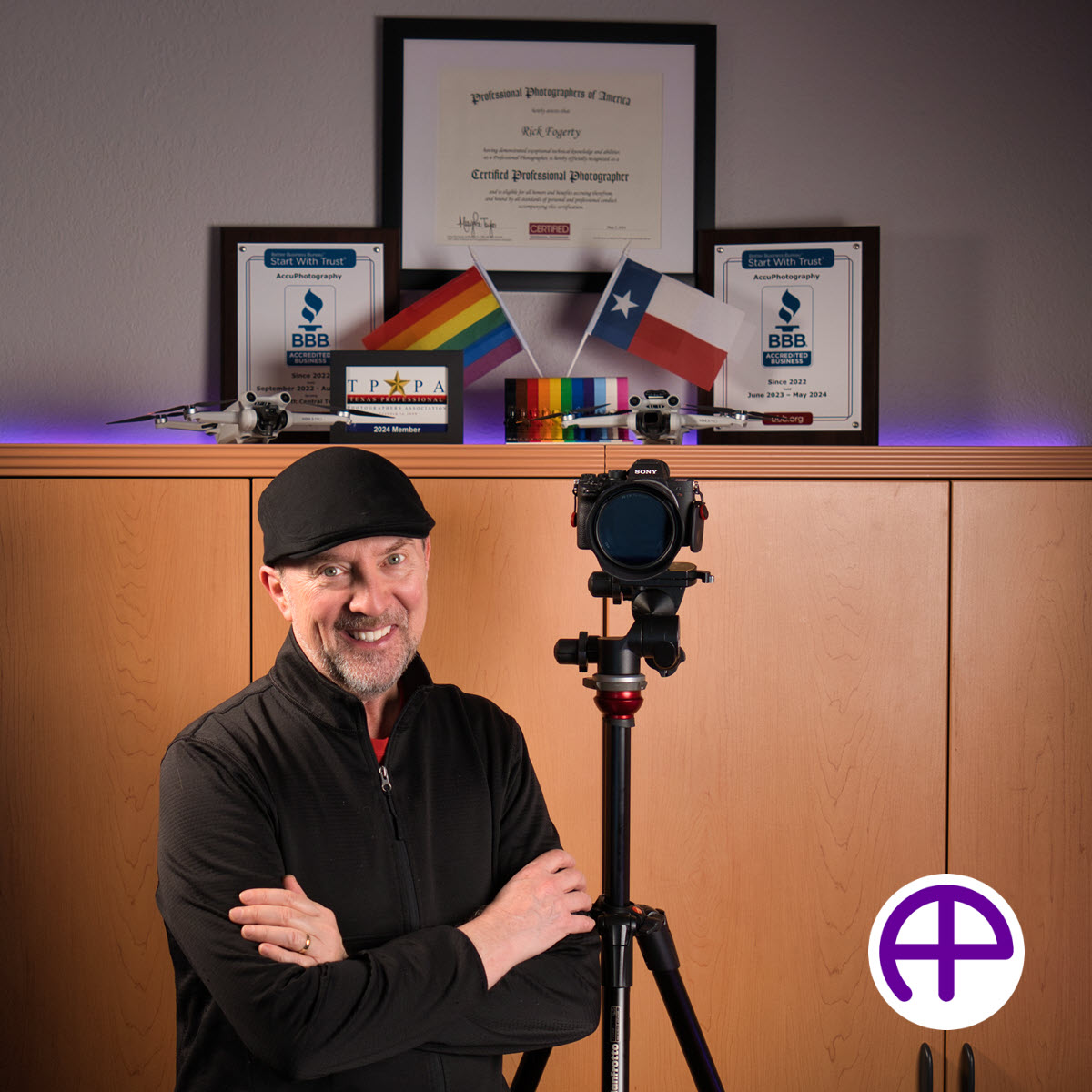 Rick fogerty, certified professional photographer, standing next to sony camera, framed certified professional photographer certificate, bbb plaques, tppa member card, and two dji mini 3 pro drones, with accuphotography logo in the image.