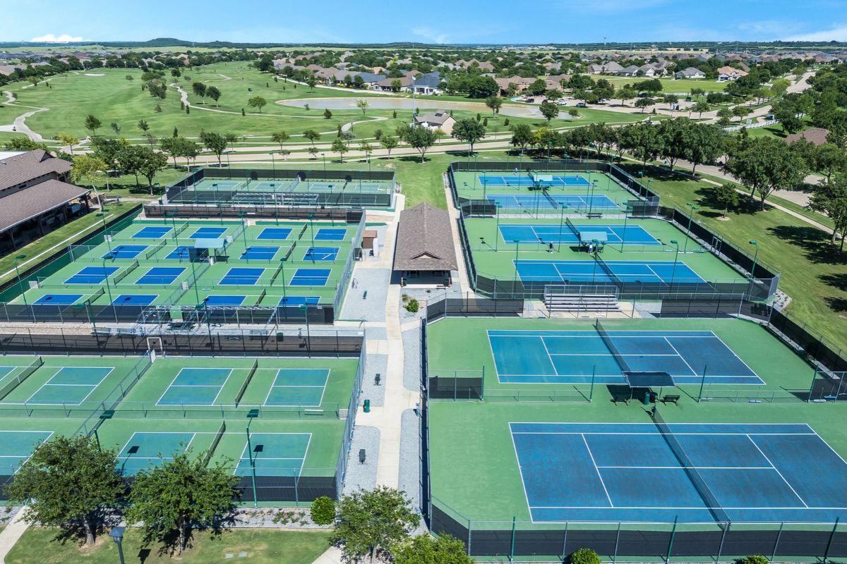Aerial drone photography of outdoor tennis and pickleball courts surrounded by green spaces at a residential community in dallas, texas.